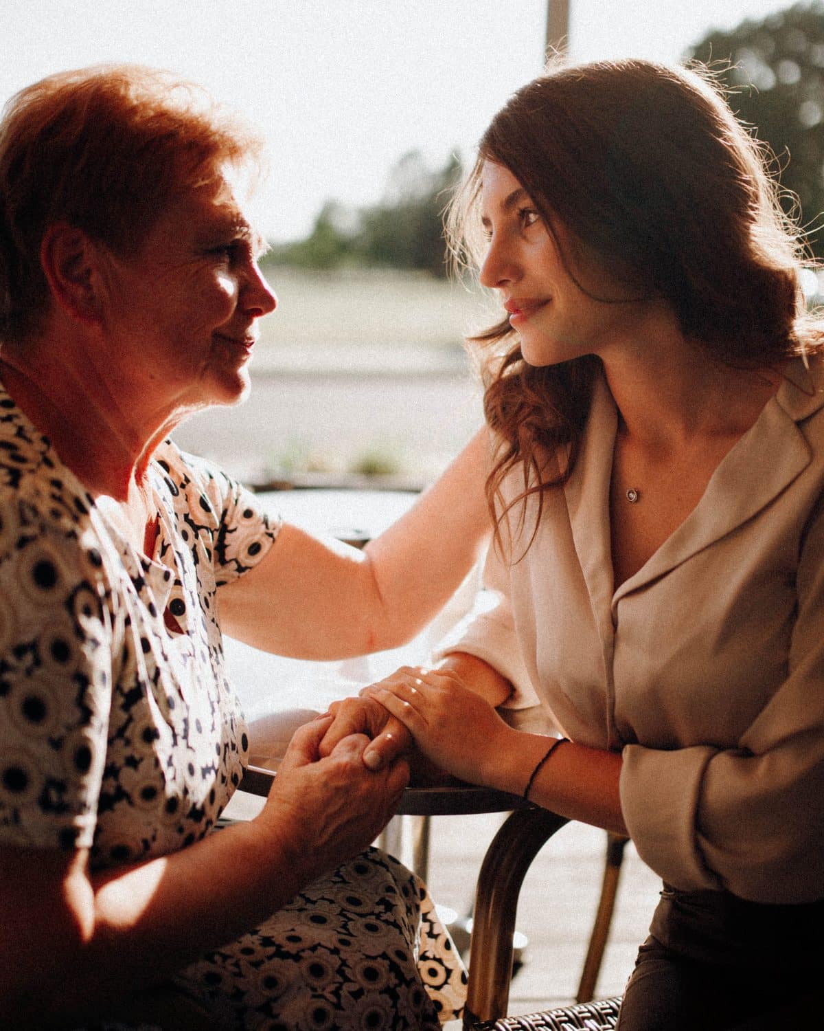 An adult daughter and her elderly mother sitting close together and looking at each other.